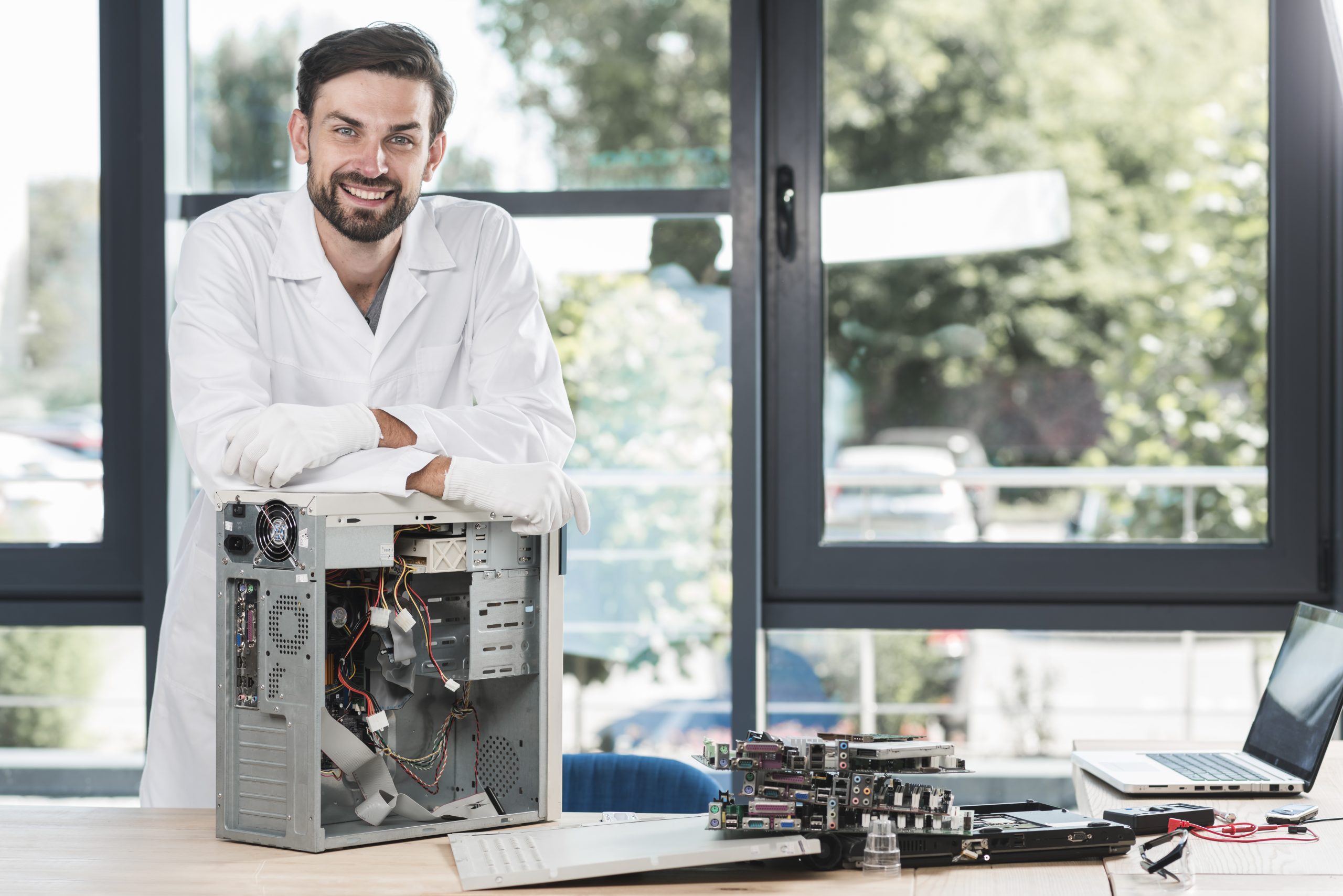 Technician at a bright workbench beside an opened desktop PC and a laptop